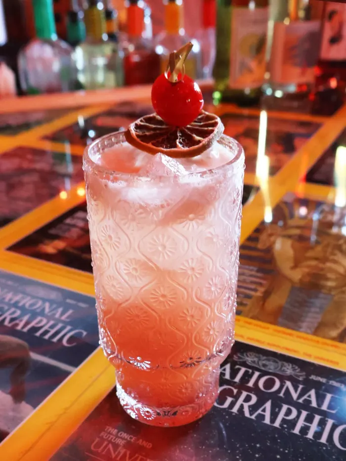 Pink White Lotus cocktail garnished with a cherry and dried orange