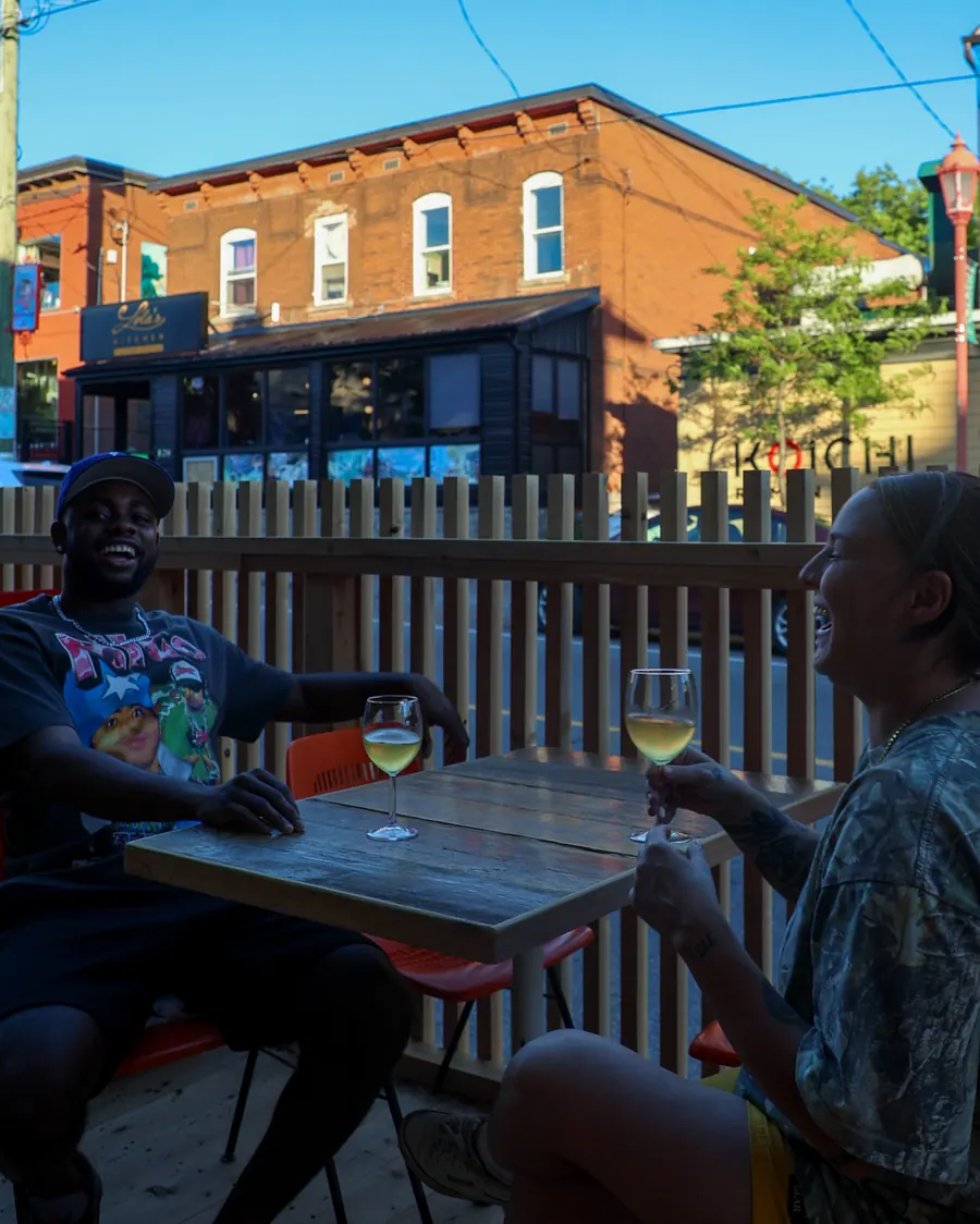 Two people having drinks on the Natural History patio in front of a red-brick building